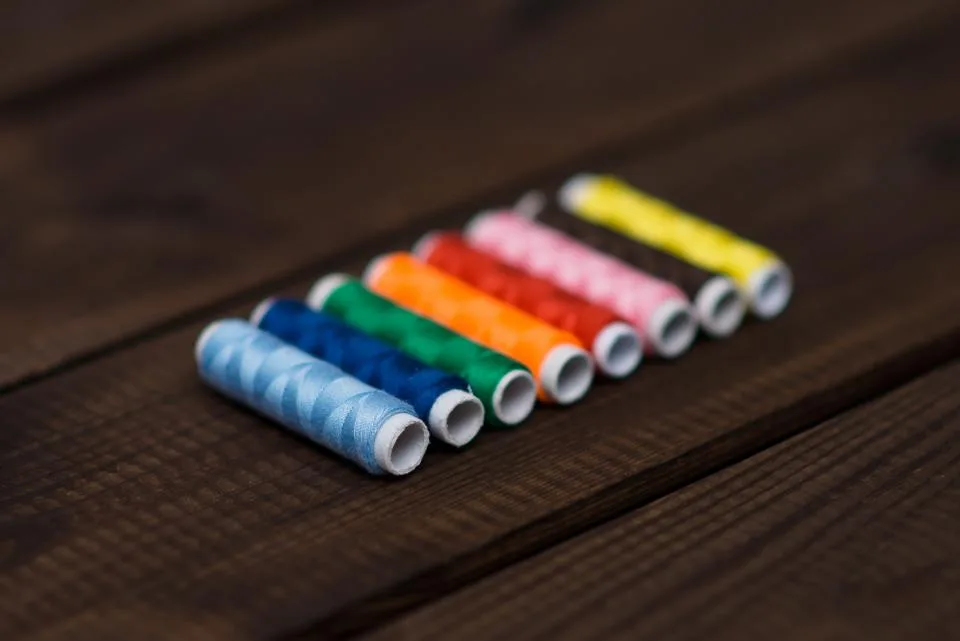 A row of colorful sewing thread spools on a dark wooden table