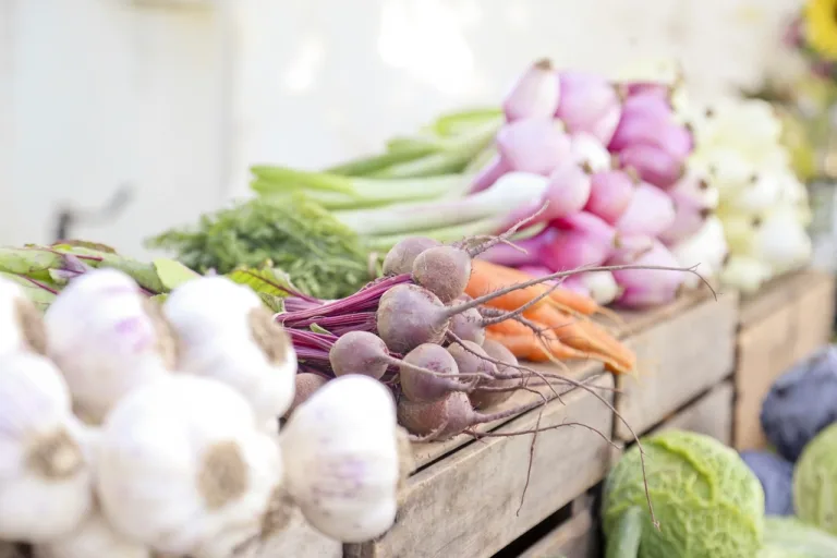 Fresh garlic, beets, carrots and onions displayed in wooden crates at a farmers market