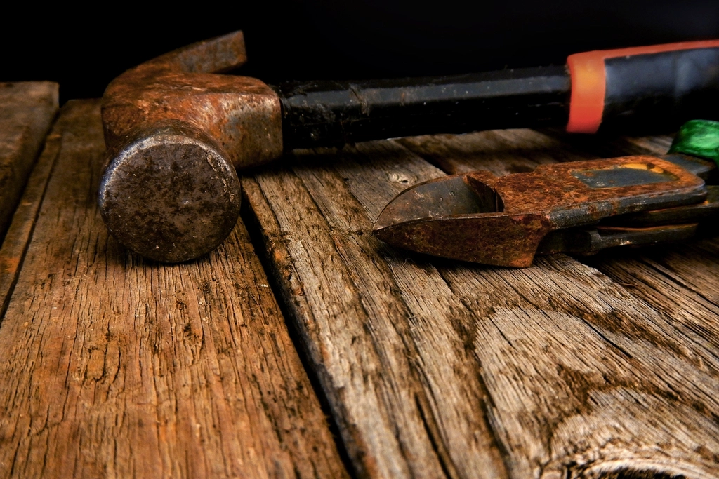 An old hammer and hand tools on a weathered wooden workbench
