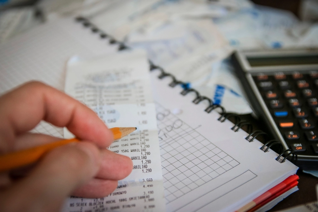 Hand holding a pencil and a receipt over a notebook beside a calculator