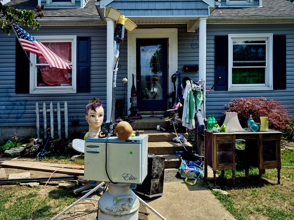 Household items set out for a yard sale on the front lawn of a small house