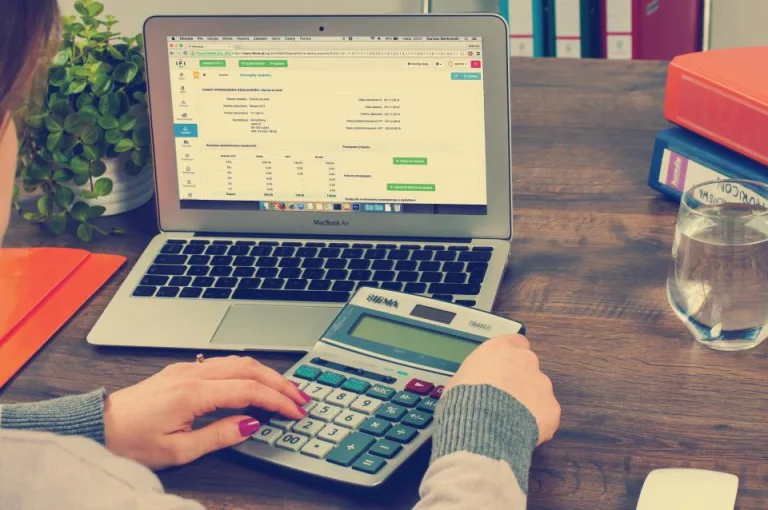 Hands using a calculator beside a laptop on a home desk