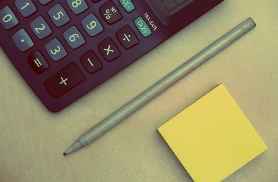 Calculator with a tax key, a pencil and a yellow sticky note on a desk