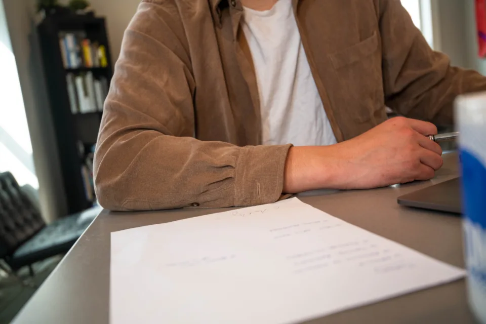 A person at a desk with a sheet of paperwork and a pen