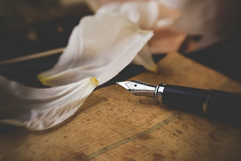 A fountain pen resting on an old document beside soft white petals