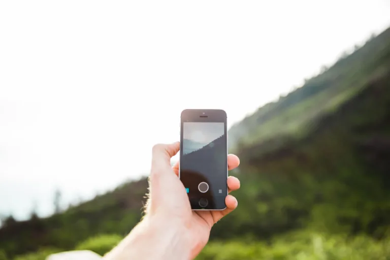 A hand holding a smartphone outdoors with green hills in the background