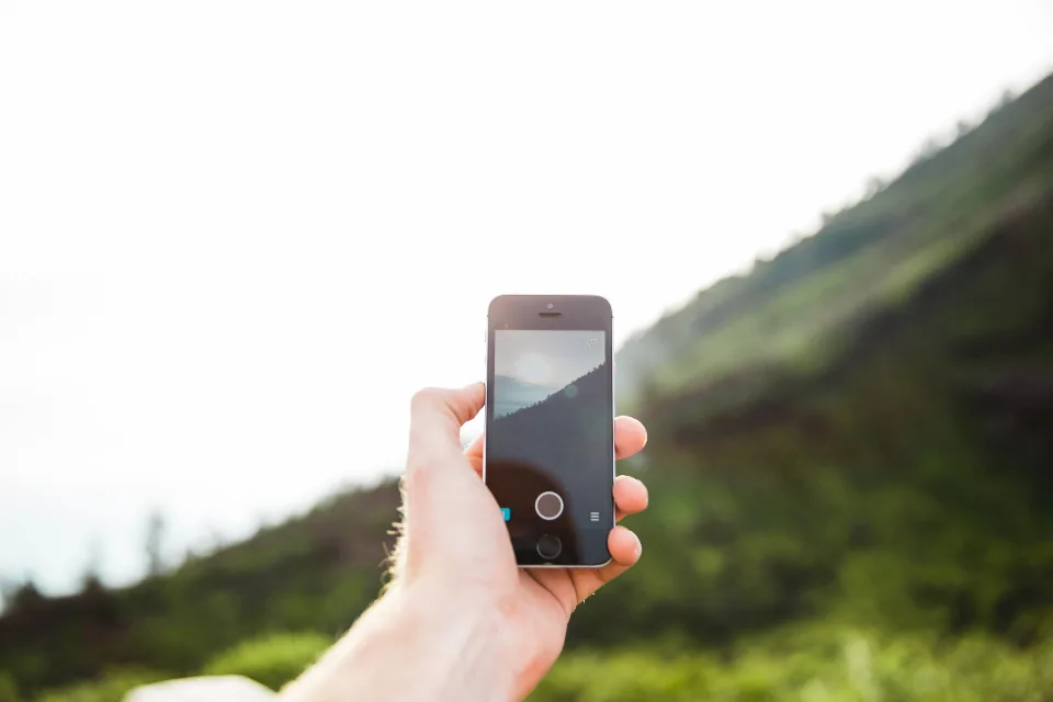 A hand holding a smartphone outdoors with green hills in the background