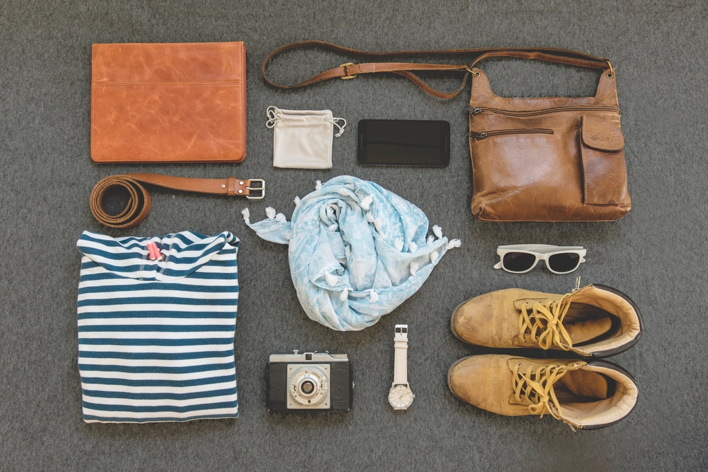 Clothing, shoes, a bag and a camera laid out neatly on a plain gray background