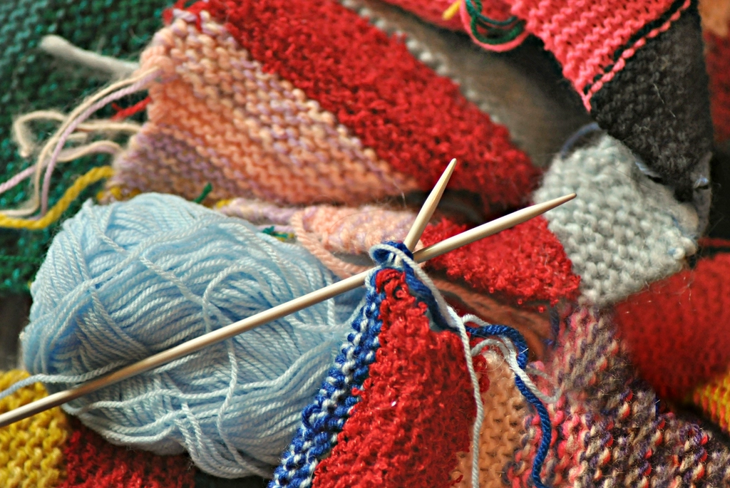 Knitting needles and a ball of light blue yarn on a colorful knitted blanket
