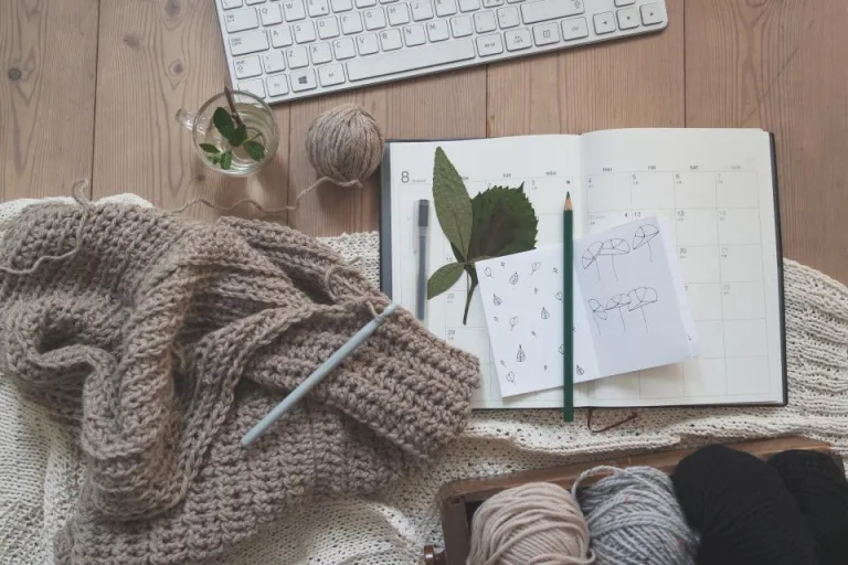Knitted wool, balls of yarn and a notebook with pencils on a wooden table