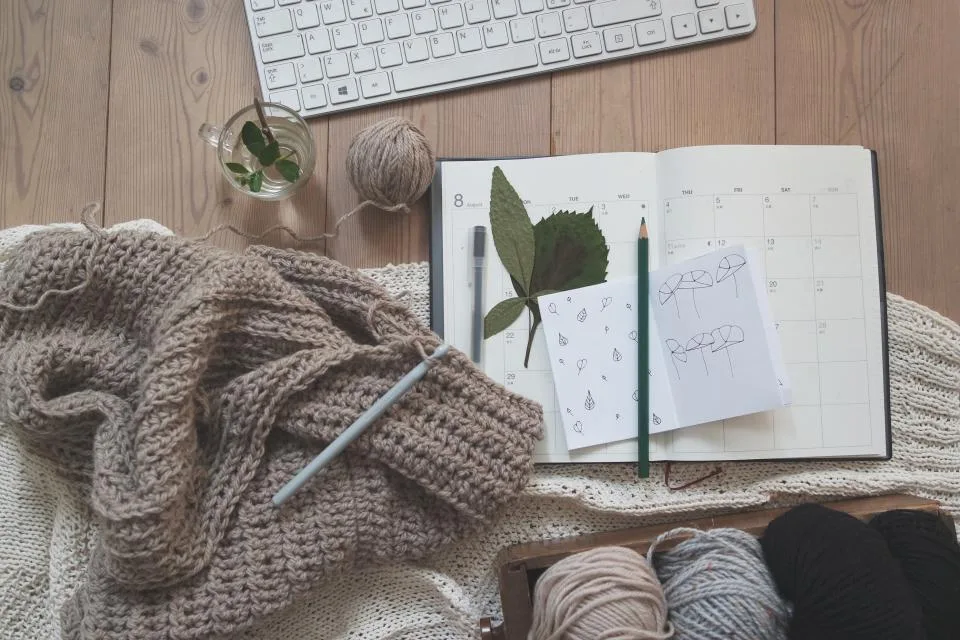 Knitted wool, balls of yarn and a notebook with pencils on a wooden table