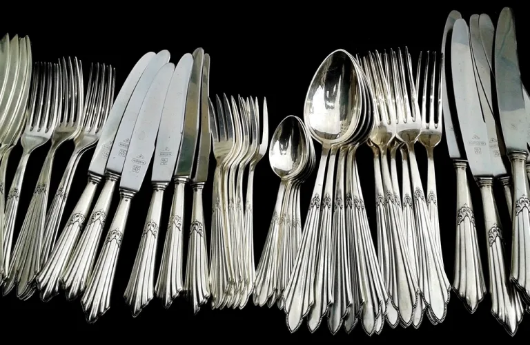 Rows of old silver forks, knives and spoons laid out on a dark background