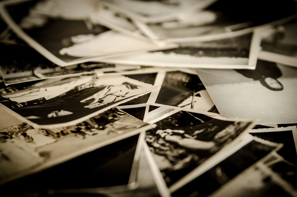 A pile of old black-and-white photographs spread across a table