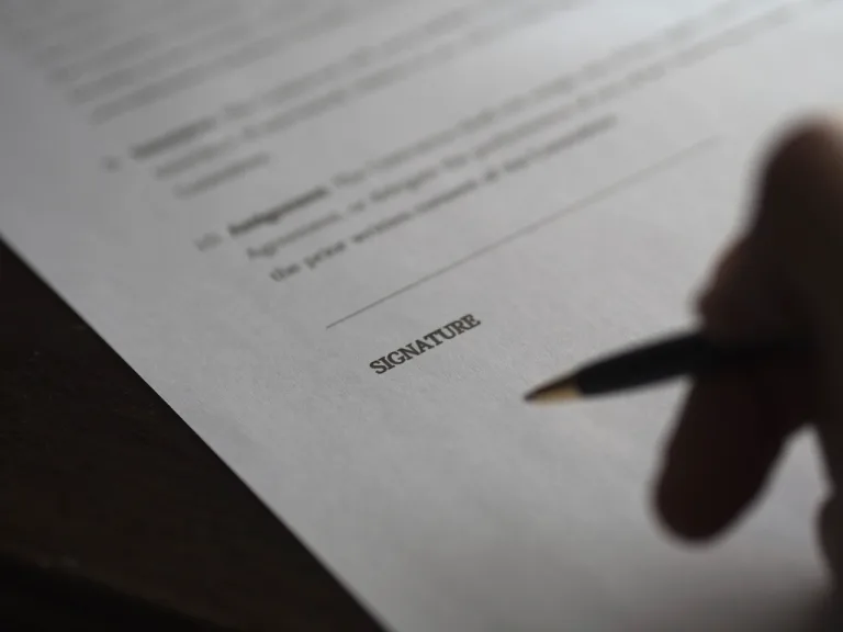A hand with a pen about to sign a printed agreement