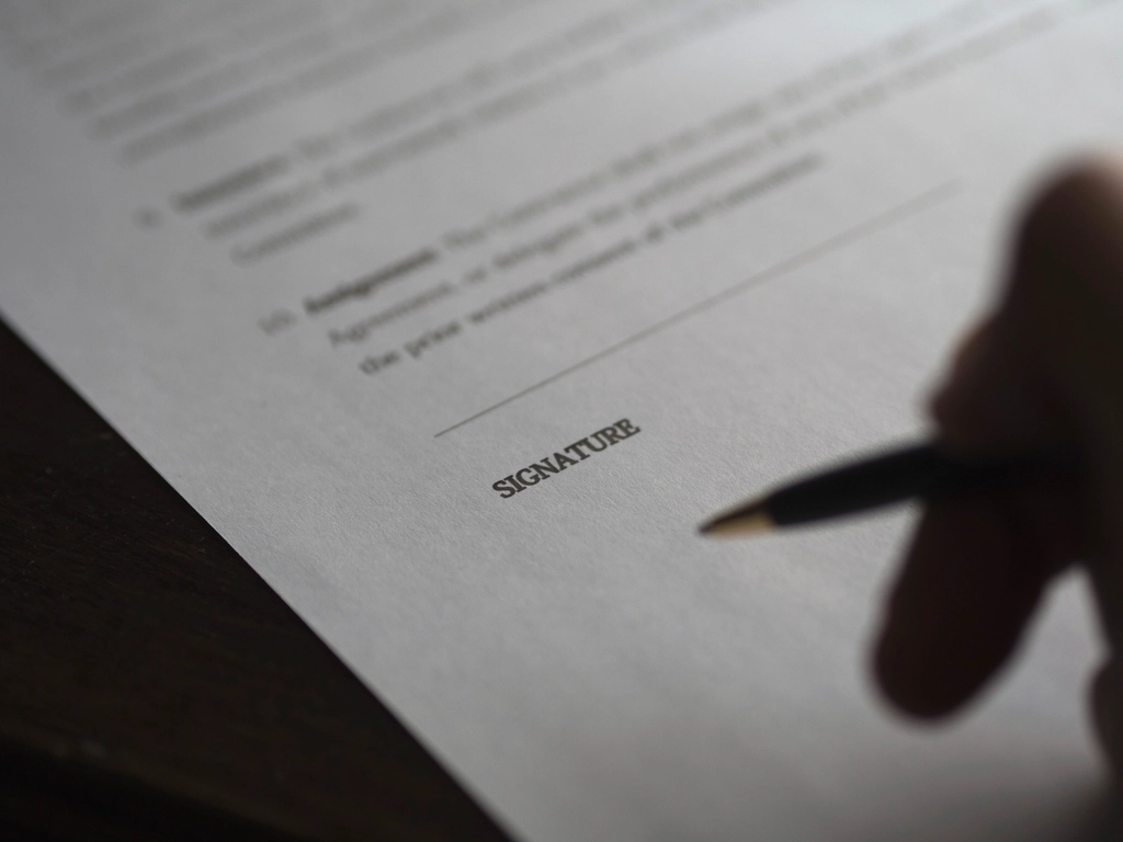A hand with a pen about to sign a printed agreement