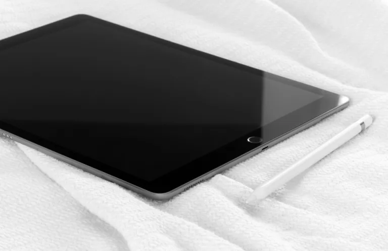 A tablet computer and stylus resting on a soft white blanket