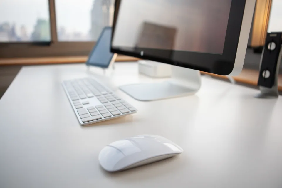 A tidy home office desk with a computer screen, keyboard and mouse by a window