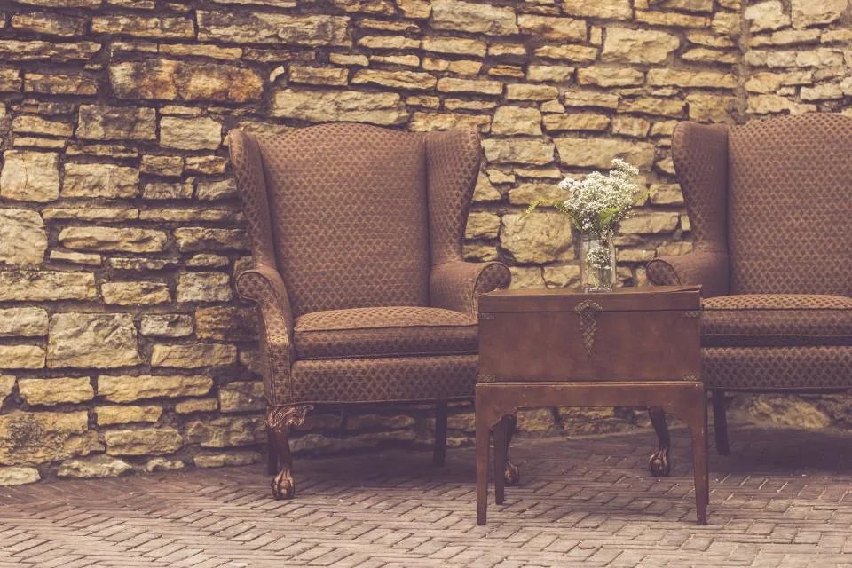 Two vintage armchairs and a small wooden chest against a stone wall