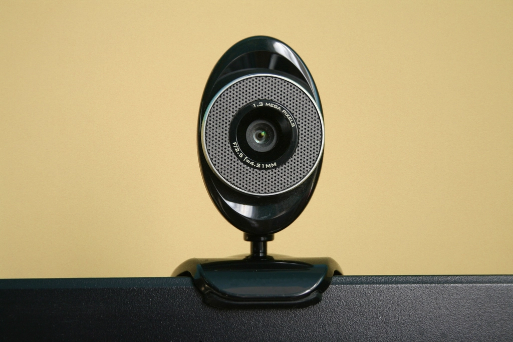 A small webcam perched on top of a computer screen against a warm yellow wall
